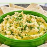 A bowl of creamy humus surrounded by pita bread slices.