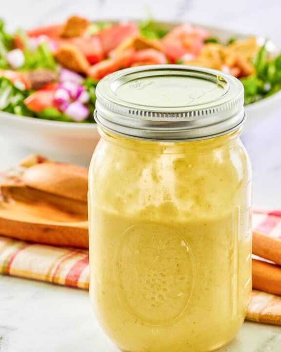 Green onion salad dressing in a mason jar and a salad behind it.