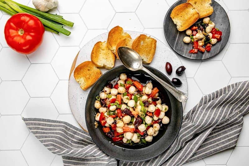 Homemade marinated mozzarella balls in a bowl and on a plate with toasted bread.
