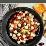 Overhead view of marinated mozzarella balls in a black bowl and a kitchen towel next to it.