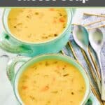 Homemade cheddar cheese soup in two soup crocks and two spoons on napkins.