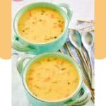 Two bowls of cheddar cheese soup and two spoons next to them.