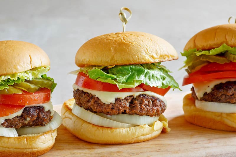 Three copycat Culver's butter burgers with toppings on a wood board.