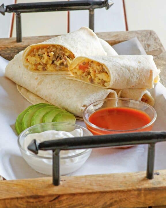 Copycat McDonald's breakfast burrito on a tray with sour cream, salsa, and avocado.