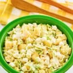 A bowl of pineapple coleslaw and salad tongs behind it.