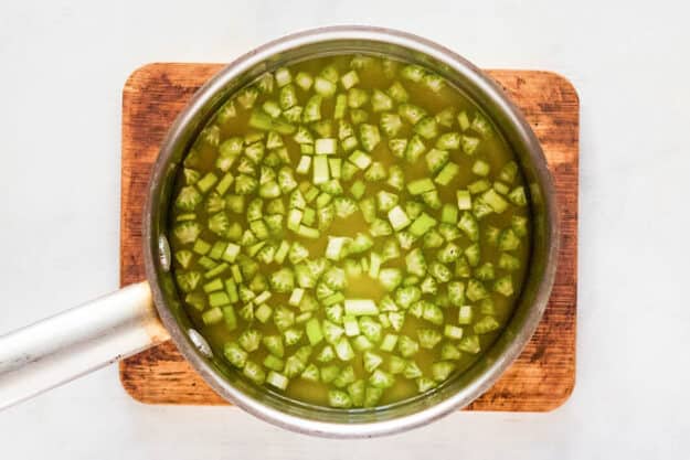 Celery poached in chicken broth in a pan.
