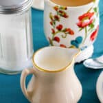 Homemade amaretto coffee creamer, a cup of coffee, and sugar.