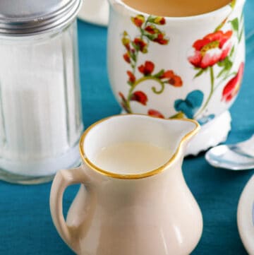 Homemade amaretto coffee creamer, a cup of coffee, and sugar.