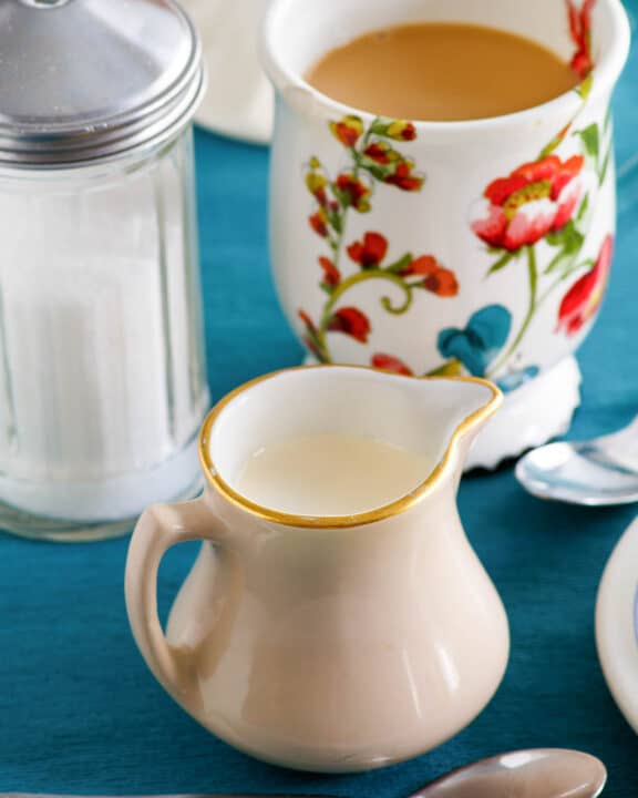 Homemade amaretto coffee creamer, a cup of coffee, and sugar.