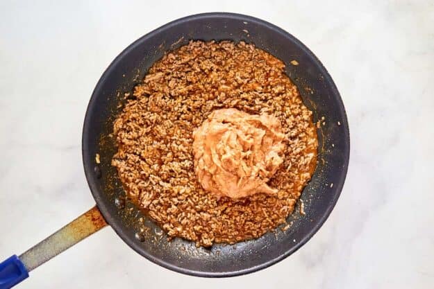 Cooked taco seasoned ground beef and refried beans in a skillet.