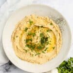Overhead view of homemade garlic hummus, garlic bulb, lemon, and parsley.