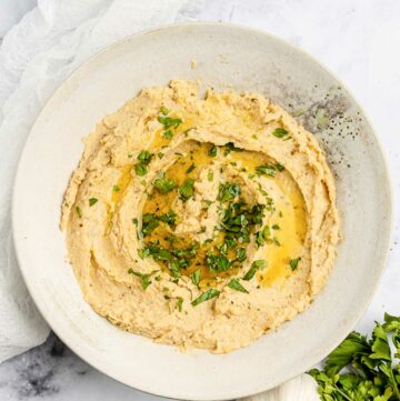 Overhead view of homemade garlic hummus, garlic bulb, lemon, and parsley.