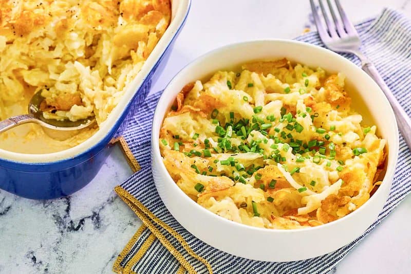A bowl of hashbrown casserole with cornflakes next to the casserole.