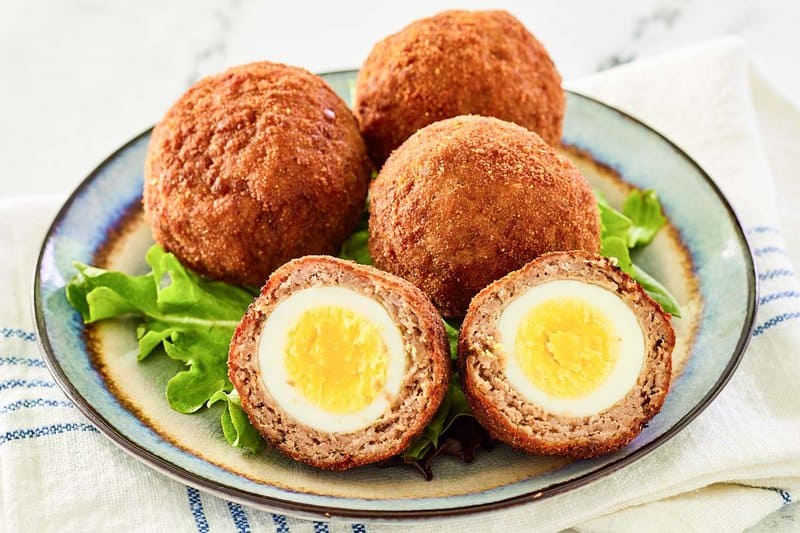 Four homemade Scotch eggs on a plate.