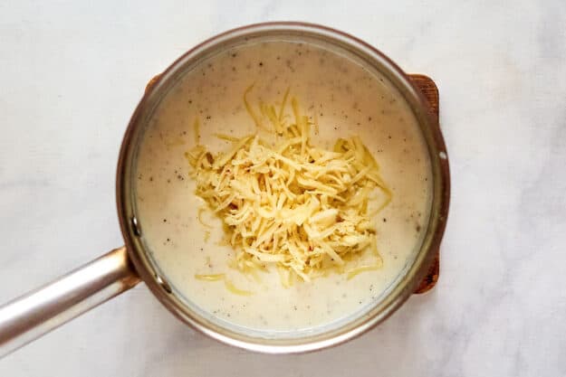 Adding cheese to white sauce for carbonara.