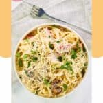 Homemade Olive Garden carbonara in a bowl and a fork on a napkin next to it.