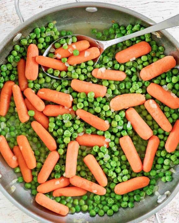 Buttery peas and carrots and a spoon in a skillet.