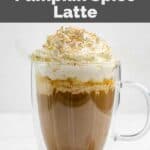 Homemade Starbucks pumpkin spice latte on a coaster and a whole nutmeg seed beside it.