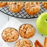 Homemade apple muffins, cinnamon sticks, and an apple.