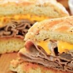 Copycat Arby's beef and cheddar sandwich cut in half and on a wood board.