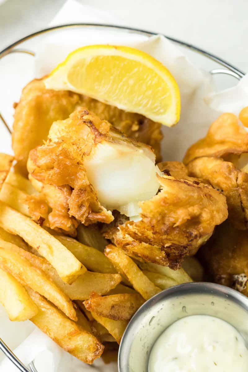 Beer battered fish and chips, tartar sauce, and lemon wedge in a serving basket.