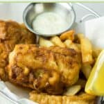 Beer battered fish and chips and a small cup of tartar sauce in a wire serving basket.