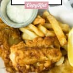 Beer battered fish and chips and tartar sauce in a wire serving basket.