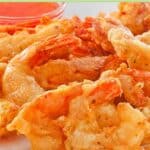 Beer battered fried shrimp and a bowl of dipping sauce on a plate.