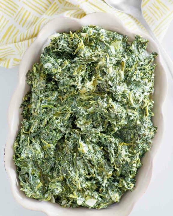 Copycat Boston Market creamed spinach in a baking dish and a serving spoon next to it.