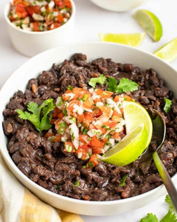 Copycat Chili's black beans garnished with pice de gallo and lime wedges.