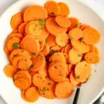 Cooked carrots on a plate and a bowl of chopped fresh parsley.