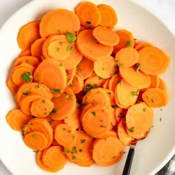 Cooked carrots on a plate and a bowl of chopped fresh parsley.