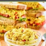 A small bowl of curried chicken salad and sandwiches behind it.