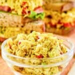 A bowl of curried chicken salad and sandwich behind it.