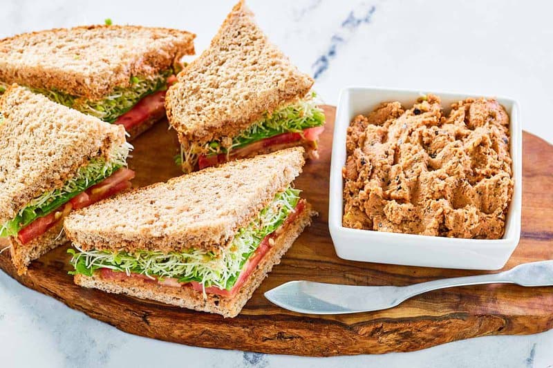 Homemade Loma Linda sandwich spread and sandwiches next to it on a wood board.