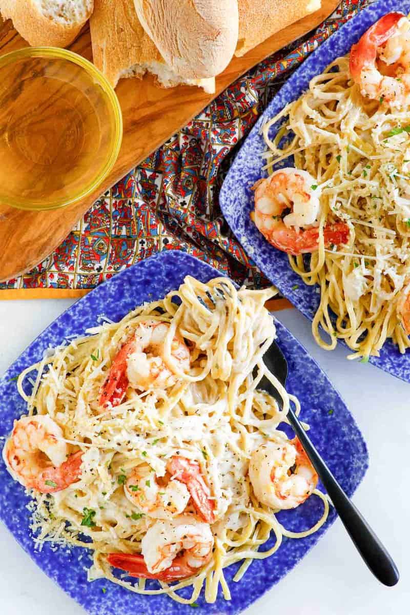 Copycat Olive Garden shrimp alfredo on two plates and bread on a wood board.