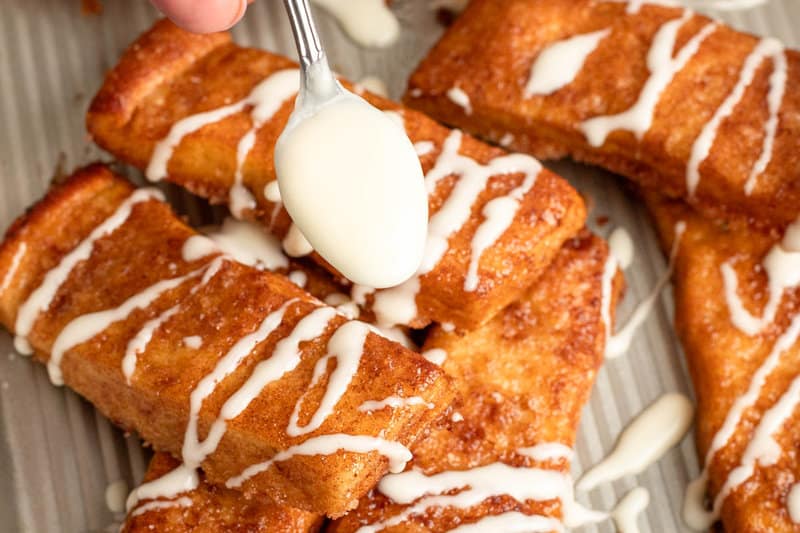 Drizzling cream cheese icing on copycat Pizza Hut cinnamon sticks.