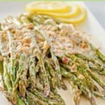 Sauteed asparagus spears with lemon cream sauce and lemon slices on a platter.