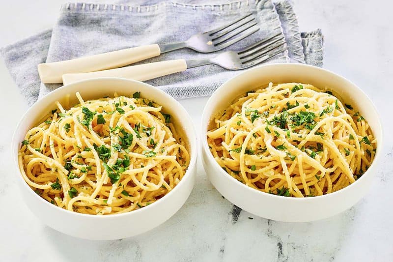 Two forks and two bowls of copycat Spaghetti warehouse spaghetti with garlic butter.