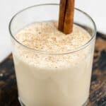 A glass of homemade spiked eggnog with a cinnamon stick stirrer.
