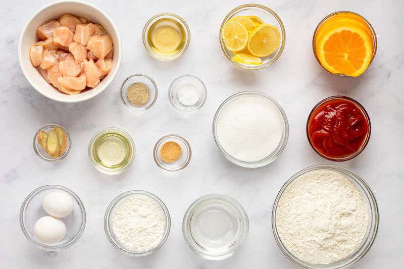 Sweet and sour chicken ingredients in bowls on a marble surface.