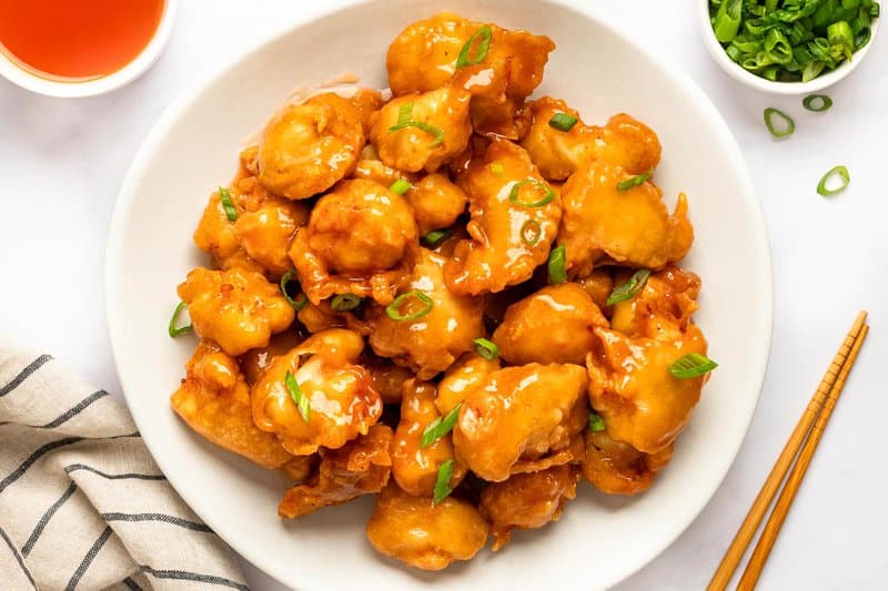 Sweet and sour chicken on a plate and chopsticks next to it.