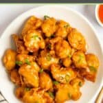 Sweet and sour chicken garnished with sliced green onions on a plate.