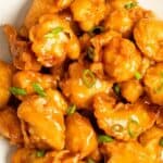 Homemade sweet and sour chicken garnished with green onions.