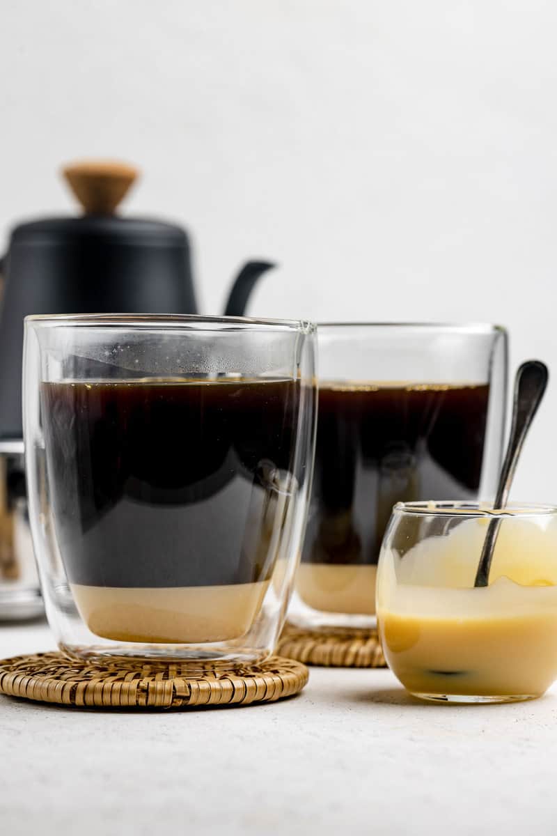 Vietnamese coffee in two mugs and a small bowl of sweetened condensed milk.