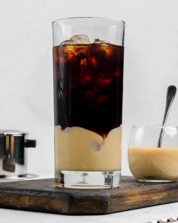Vietnamese iced coffee in a tall glass and a small bowl of sweetened condensed milk.