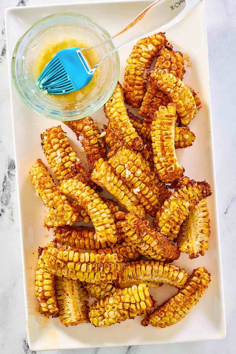 A fryer corn ribs and a bowl of garlic butter on a large platter.