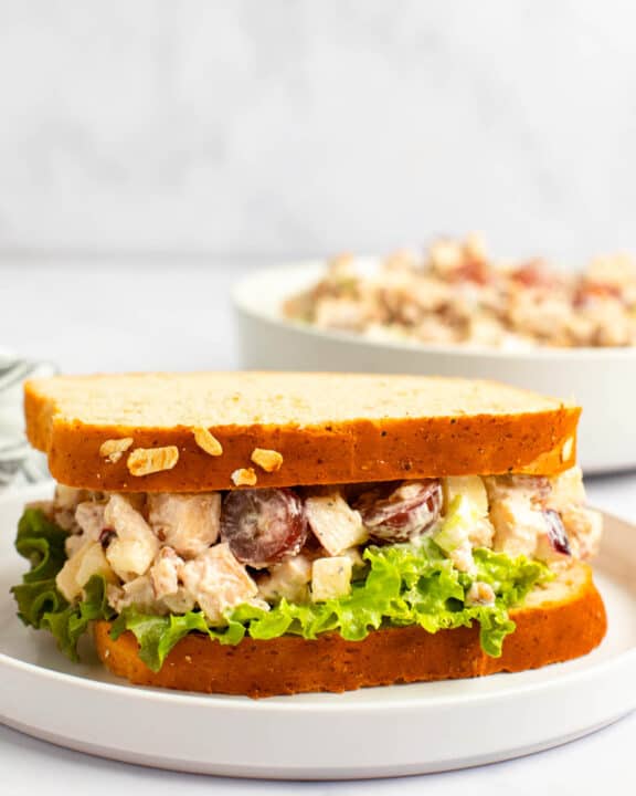 Copycat Arby's pecan chicken salad sandwich on a plate and the salad in a bowl behind it.