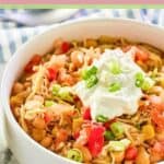 A bowl of crockpot white chicken chili garnished with sour cream and sliced green onions.