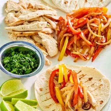 Grilled chicken fajitas, a cup of chopped cilantro, and lime wedges.